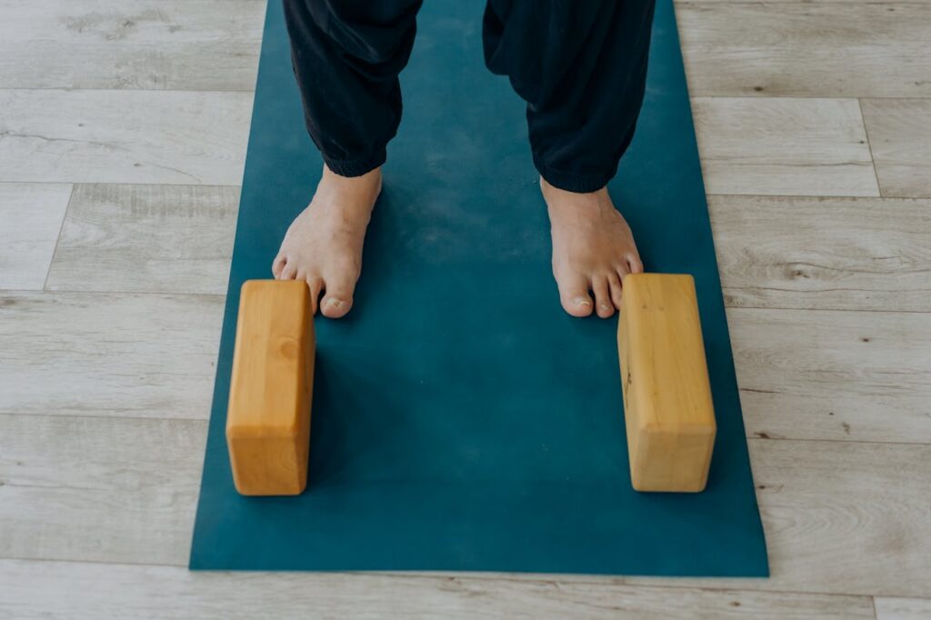 Close-up of feet on a yoga mat beside wooden blocks indoors.