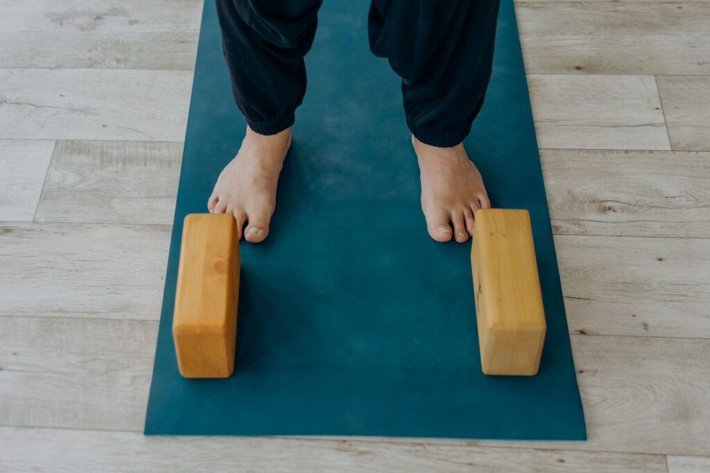 Close-up of feet on a yoga mat beside wooden blocks indoors.