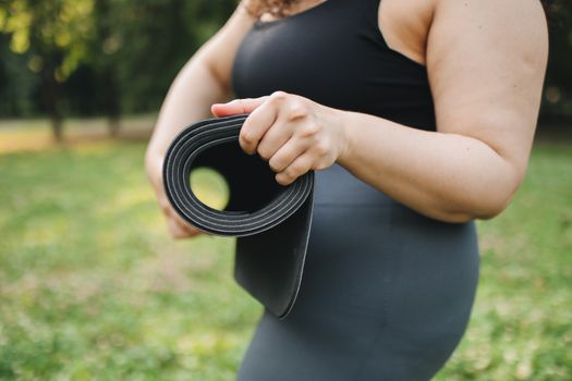Close-up of a woman holding a yoga mat in a sunny outdoor park setting.